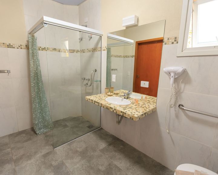 Accessible bathroom with a roll-in glass shower, an open wall-mounted sink, and grab bars