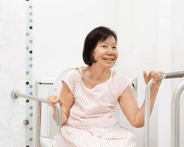 Older woman holding bathroom grab bars beside a toilet