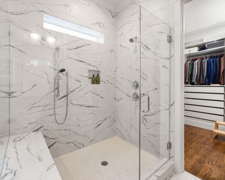 Walk-in shower with marble-look tile, a built-in bench, and a frameless glass enclosure